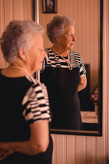 An old lady standing in front of the mirror